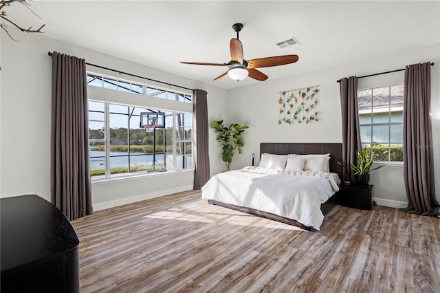 bedroom featuring a water view, light hardwood / wood-style floors, and ceiling fan