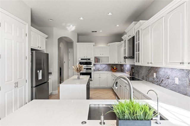 kitchen featuring a center island, white cabinets, light tile patterned flooring, backsplash, and appliances with stainless steel finishes