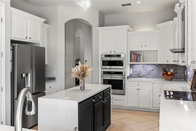 kitchen with stainless steel appliances, a center island, decorative backsplash, light tile patterned floors, and white cabinetry