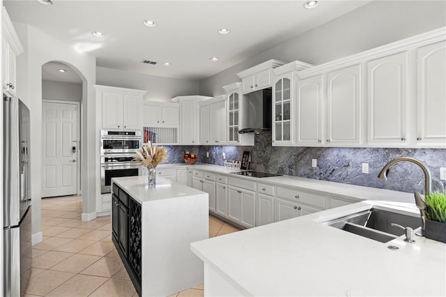 kitchen featuring stainless steel appliances, wall chimney exhaust hood, white cabinets, and a kitchen island with sink