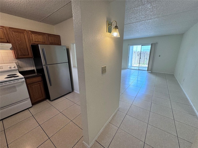 kitchen with tasteful backsplash, stainless steel refrigerator, light tile patterned floors, and white range with electric cooktop