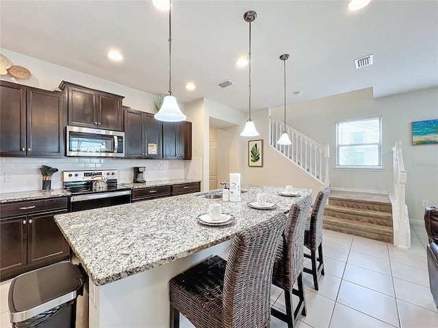 kitchen with pendant lighting, a kitchen island with sink, dark brown cabinets, and stainless steel appliances