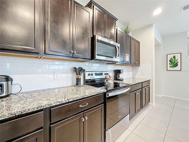 kitchen with decorative backsplash, light stone countertops, stainless steel appliances, and dark brown cabinets