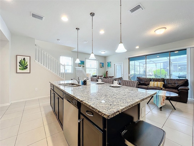 kitchen with hanging light fixtures, a center island with sink, dishwasher, sink, and light stone counters