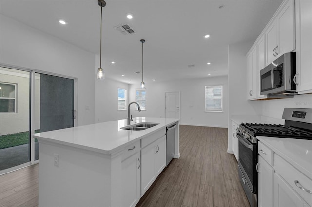 kitchen featuring sink, hanging light fixtures, an island with sink, stainless steel appliances, and white cabinets