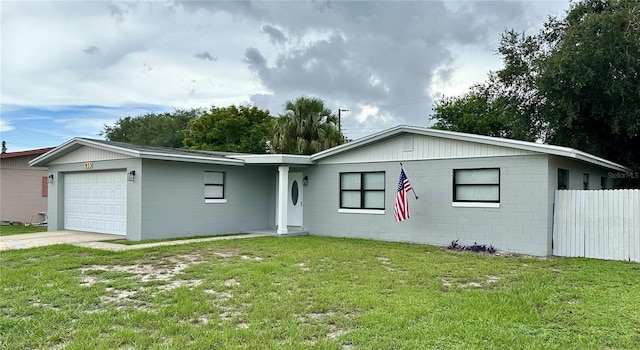 single story home featuring an attached garage, a front yard, concrete block siding, and concrete driveway