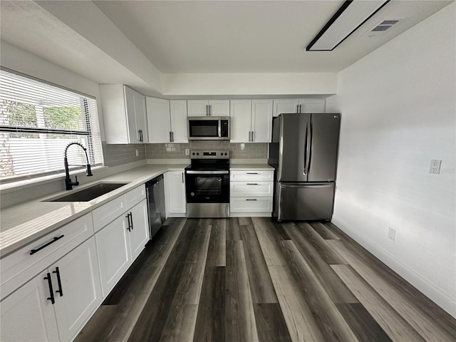 kitchen with dark wood-type flooring, backsplash, sink, white cabinets, and appliances with stainless steel finishes