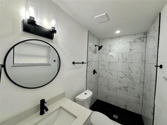 bathroom with toilet, a textured ceiling, vanity, and a tile shower