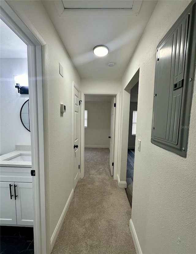 hall with electric panel, dark colored carpet, baseboards, and a sink