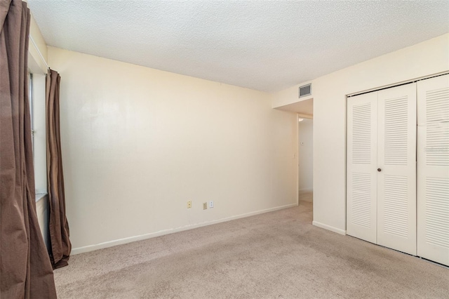 unfurnished bedroom featuring a closet, a textured ceiling, and light colored carpet