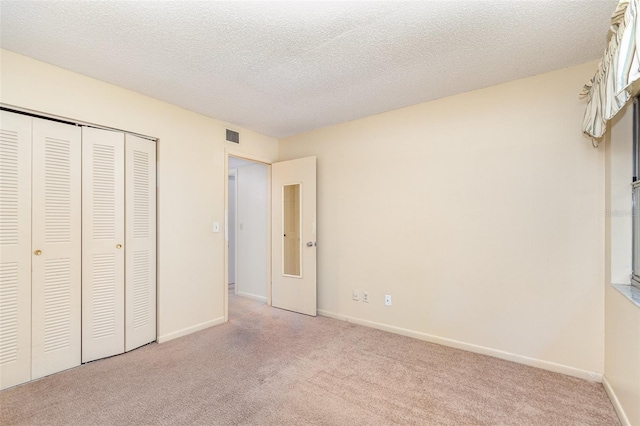 unfurnished bedroom featuring a closet, a textured ceiling, and light colored carpet