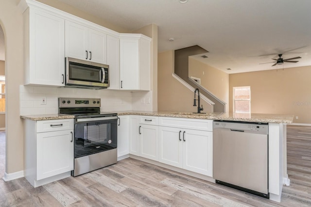 kitchen with sink, kitchen peninsula, stainless steel appliances, white cabinets, and light hardwood / wood-style flooring