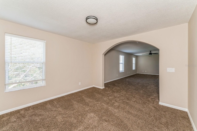 spare room featuring ceiling fan, a textured ceiling, a wealth of natural light, and dark carpet