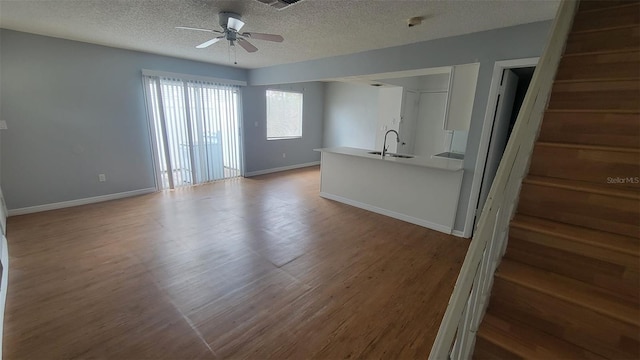 unfurnished living room featuring a textured ceiling, hardwood / wood-style flooring, sink, and ceiling fan