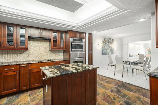 kitchen with black electric stovetop, dark stone counters, double oven, crown molding, and a kitchen island