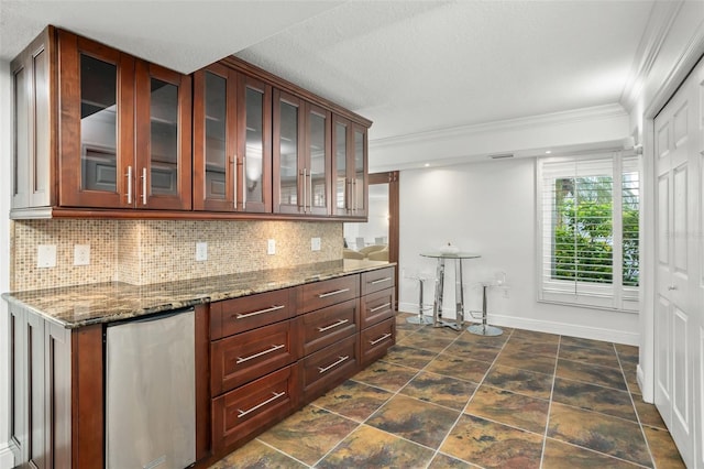 kitchen featuring a textured ceiling, crown molding, dark stone counters, and fridge