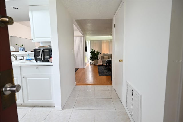 hall with sink, a textured ceiling, and light tile patterned flooring