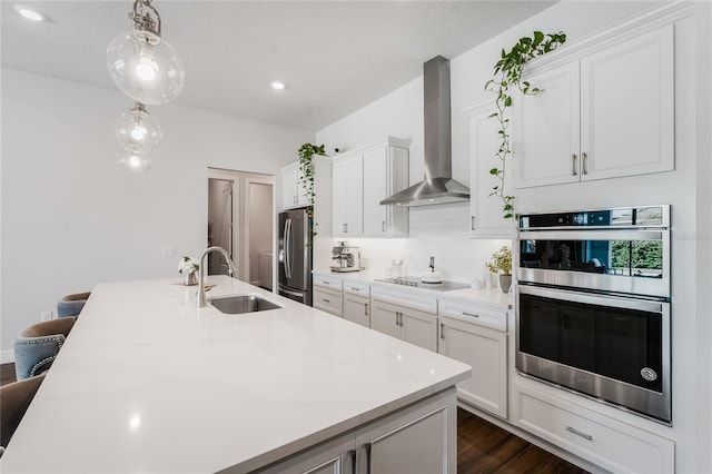 kitchen featuring hanging light fixtures, appliances with stainless steel finishes, a kitchen breakfast bar, wall chimney exhaust hood, and sink