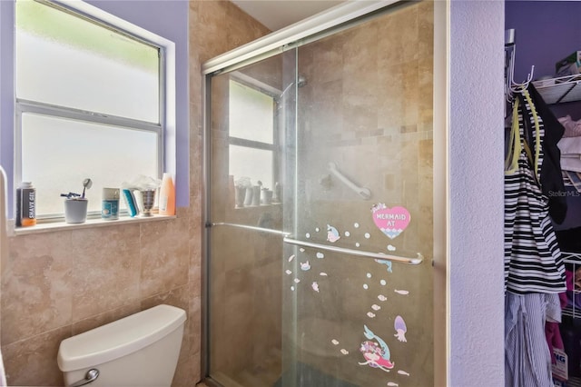 bathroom with tile walls, a shower with shower door, and toilet