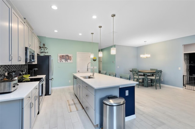 kitchen with a kitchen island with sink, sink, decorative light fixtures, light hardwood / wood-style floors, and stainless steel appliances