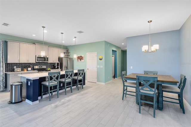 kitchen featuring gray cabinets, a kitchen island with sink, decorative light fixtures, and appliances with stainless steel finishes