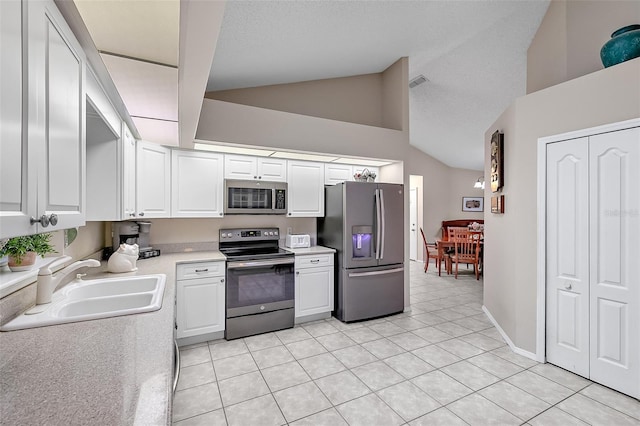 kitchen with light tile patterned floors, appliances with stainless steel finishes, white cabinetry, vaulted ceiling, and sink