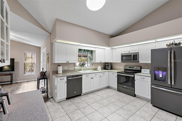 kitchen featuring stainless steel appliances, vaulted ceiling, plenty of natural light, and white cabinets