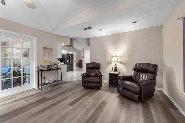 living area featuring vaulted ceiling, a textured ceiling, light hardwood / wood-style floors, and ceiling fan