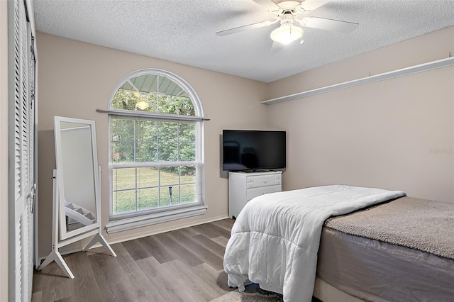 bedroom featuring ceiling fan, a textured ceiling, wood-type flooring, and multiple windows