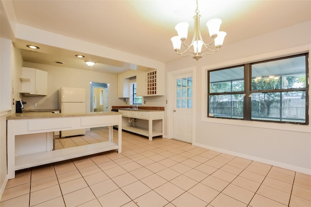 kitchen with hanging light fixtures, light tile patterned flooring, white refrigerator, a chandelier, and white cabinetry