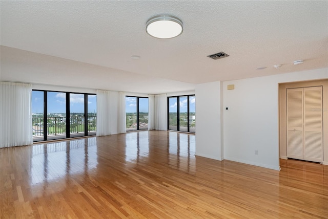 empty room with a textured ceiling, light hardwood / wood-style flooring, and a wall of windows