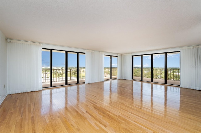 unfurnished room with a textured ceiling, light wood-type flooring, and floor to ceiling windows