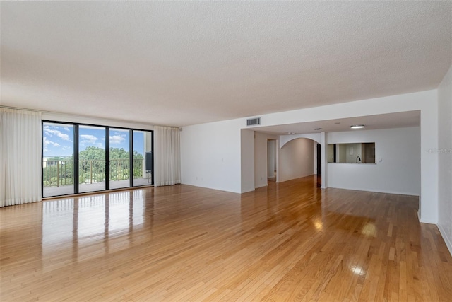 unfurnished room with a wall of windows, a textured ceiling, and light wood-type flooring