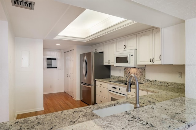 kitchen with white appliances, light stone countertops, sink, white cabinets, and light hardwood / wood-style flooring