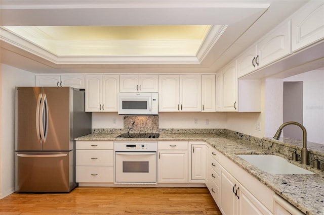 kitchen with white appliances, light hardwood / wood-style floors, a raised ceiling, and sink