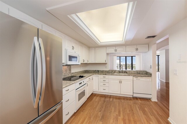 kitchen featuring white appliances, sink, light wood-type flooring, a raised ceiling, and white cabinets