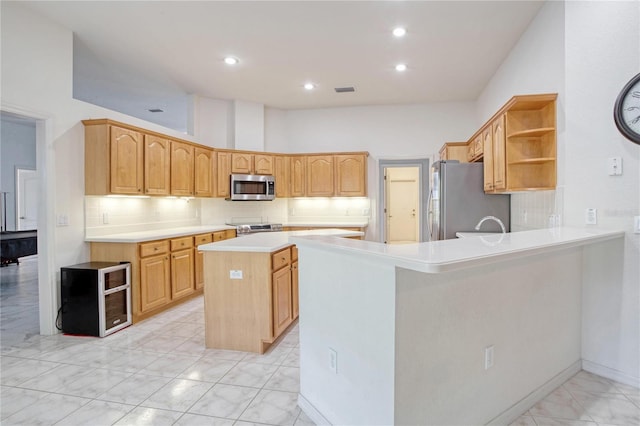 kitchen featuring kitchen peninsula, decorative backsplash, a kitchen island, light brown cabinetry, and stainless steel appliances