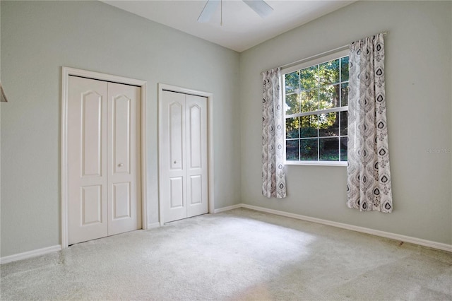 unfurnished bedroom with ceiling fan, multiple closets, and light colored carpet