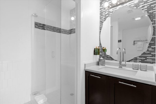 bathroom with a shower with door, vanity, and backsplash