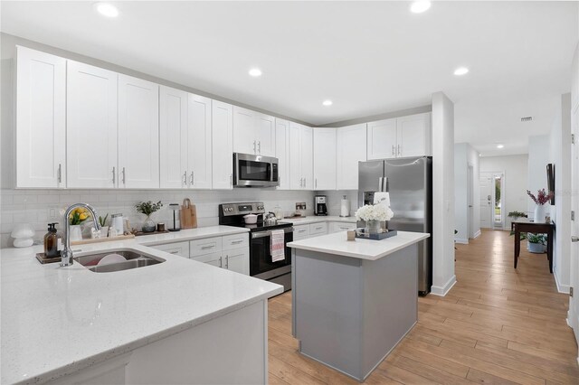 kitchen with appliances with stainless steel finishes, sink, a kitchen island, light hardwood / wood-style floors, and white cabinets