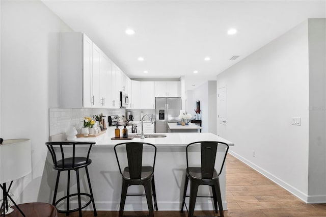 kitchen with light hardwood / wood-style floors, white cabinets, stainless steel appliances, and a kitchen breakfast bar