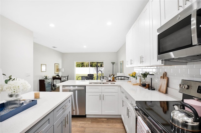 kitchen featuring appliances with stainless steel finishes, sink, kitchen peninsula, white cabinetry, and light hardwood / wood-style floors