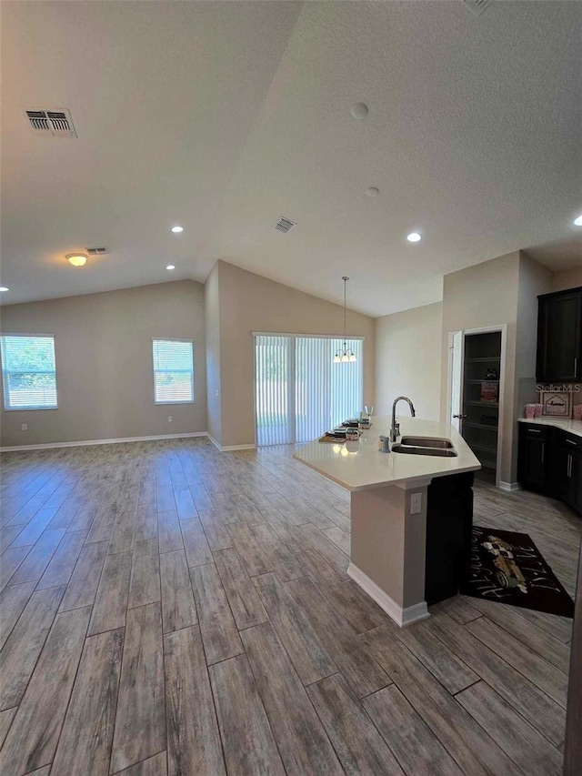 kitchen featuring light hardwood / wood-style floors, sink, an island with sink, and vaulted ceiling