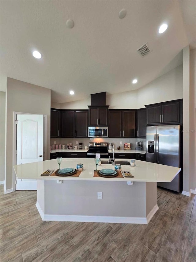 kitchen with appliances with stainless steel finishes, a kitchen island with sink, lofted ceiling, and sink