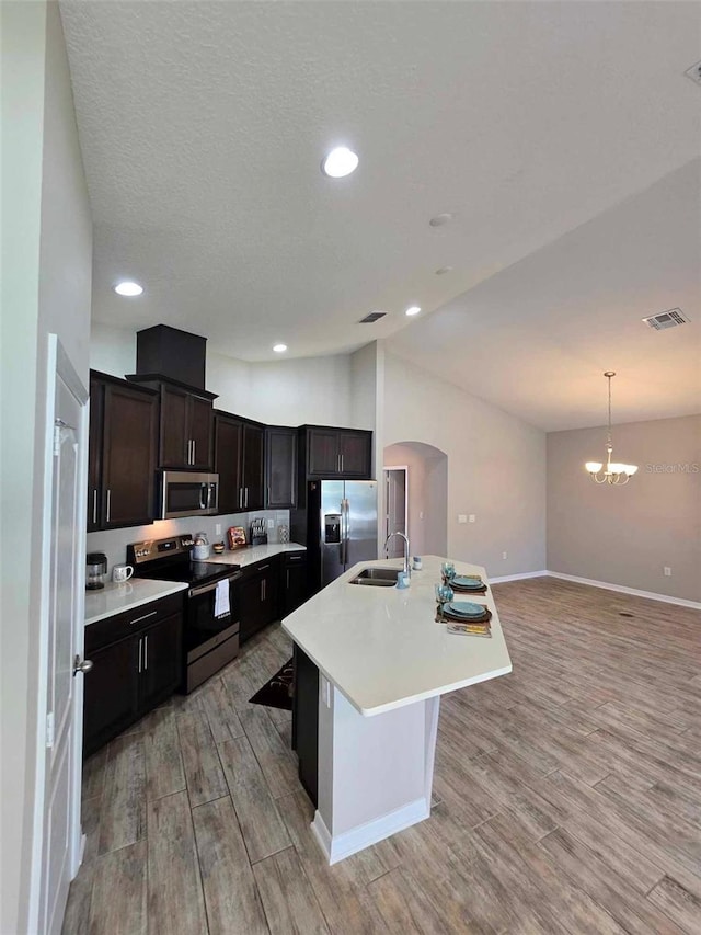 kitchen featuring sink, light hardwood / wood-style flooring, pendant lighting, a kitchen island with sink, and appliances with stainless steel finishes