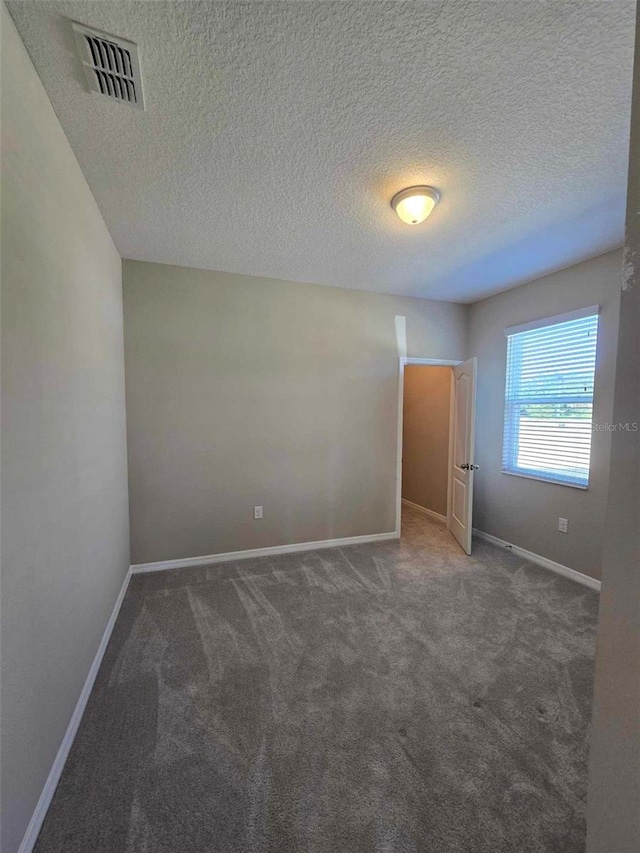 empty room with a textured ceiling and dark colored carpet