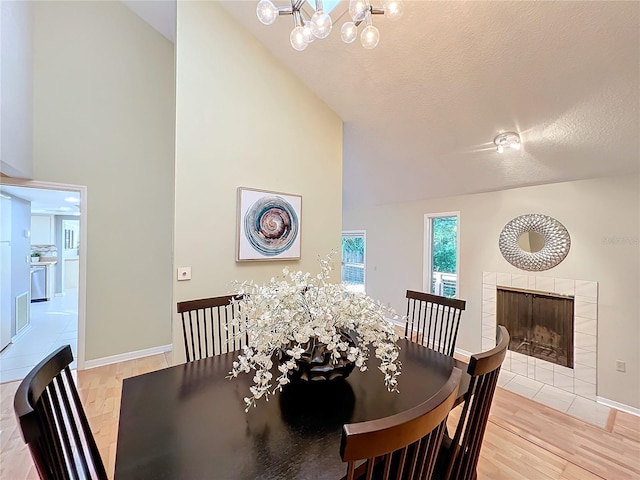 dining room with a textured ceiling, a chandelier, high vaulted ceiling, a fireplace, and light hardwood / wood-style floors