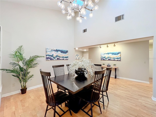 dining space with a towering ceiling, light hardwood / wood-style flooring, and a notable chandelier