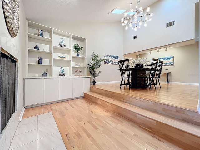 dining area with a skylight, light wood-type flooring, a textured ceiling, high vaulted ceiling, and a chandelier