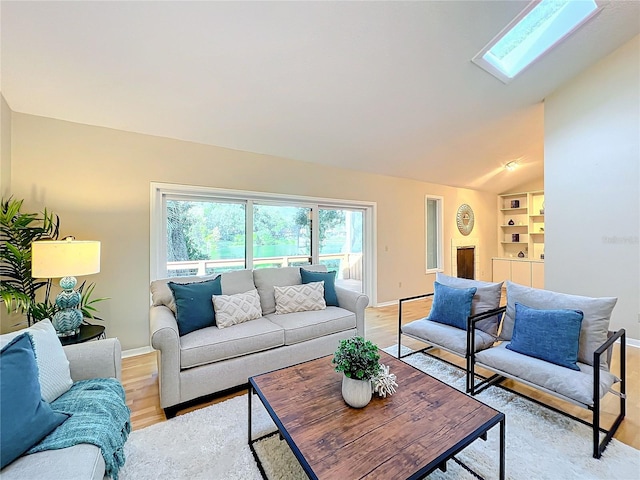 living room with vaulted ceiling with skylight, built in features, and light wood-type flooring